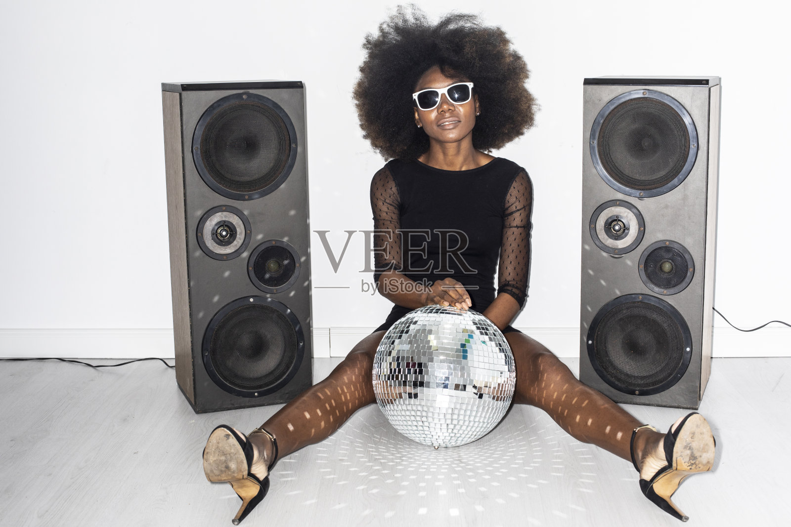 穿着黑裙戴着墨镜坐在地板上的迪斯科女郎照片摄影图片