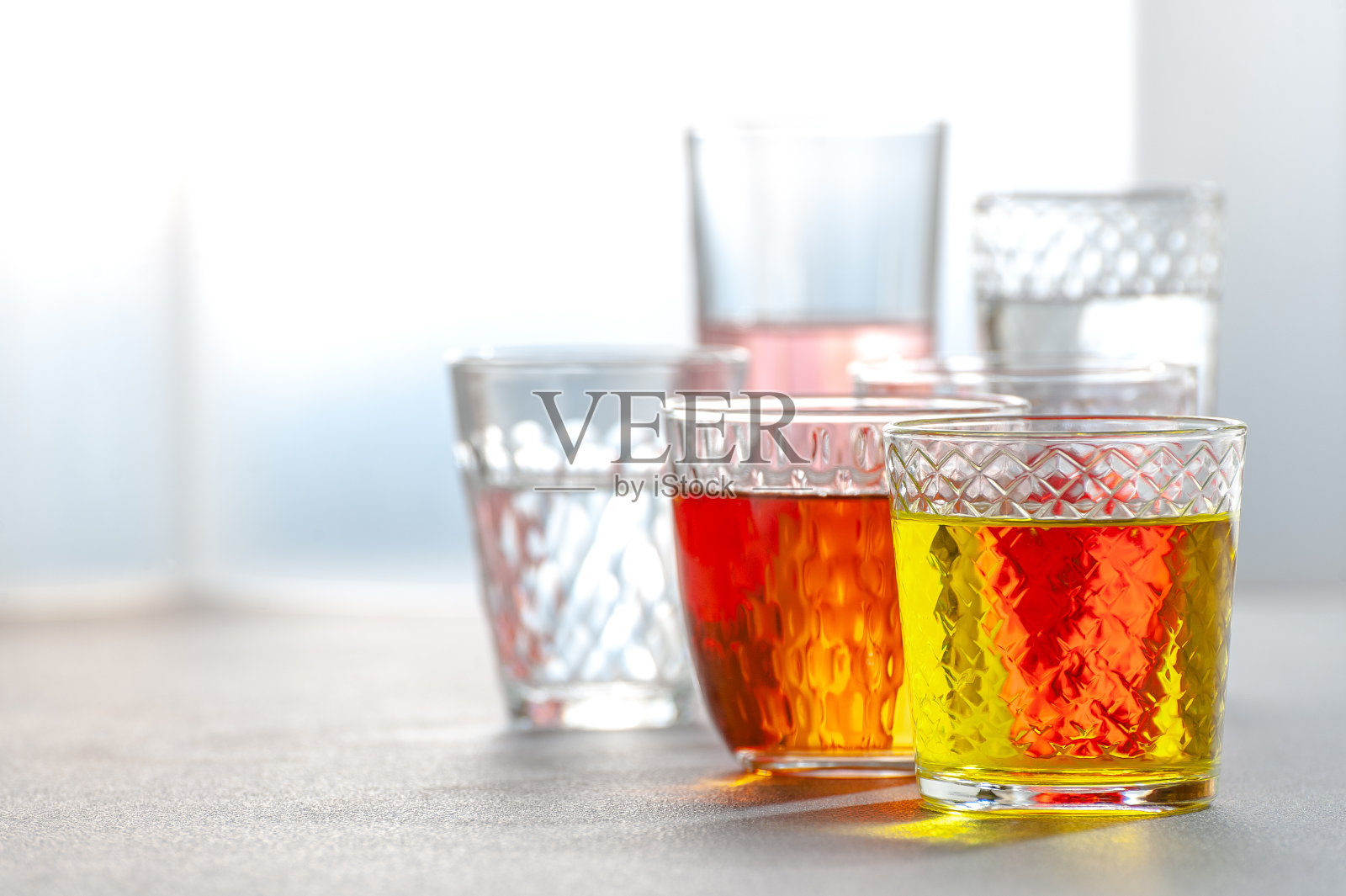 灰色的桌子上放着玻璃多面体玻璃杯里的各种柠檬汁。的背景图片。照片摄影图片