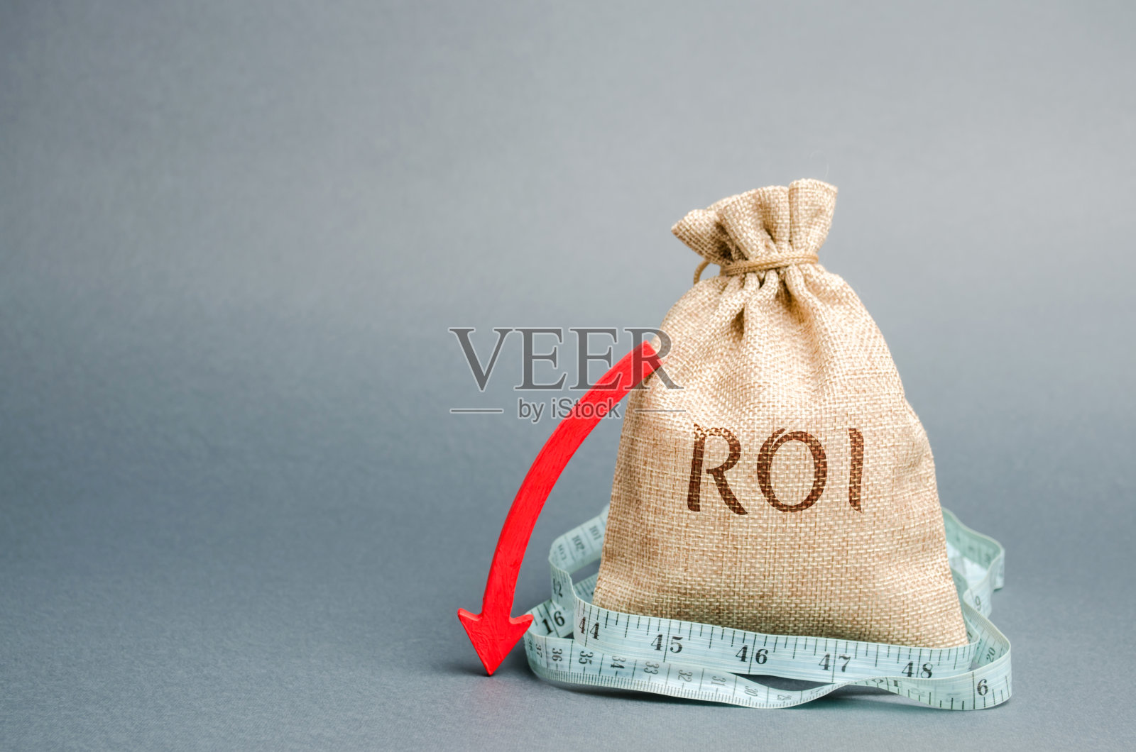 装有卷尺和“投资回报率”字样的钱袋。说明企业亏损程度的财务比率。投资回报。经济衰退。盈利能力和业绩下降。向下箭头照片摄影图片