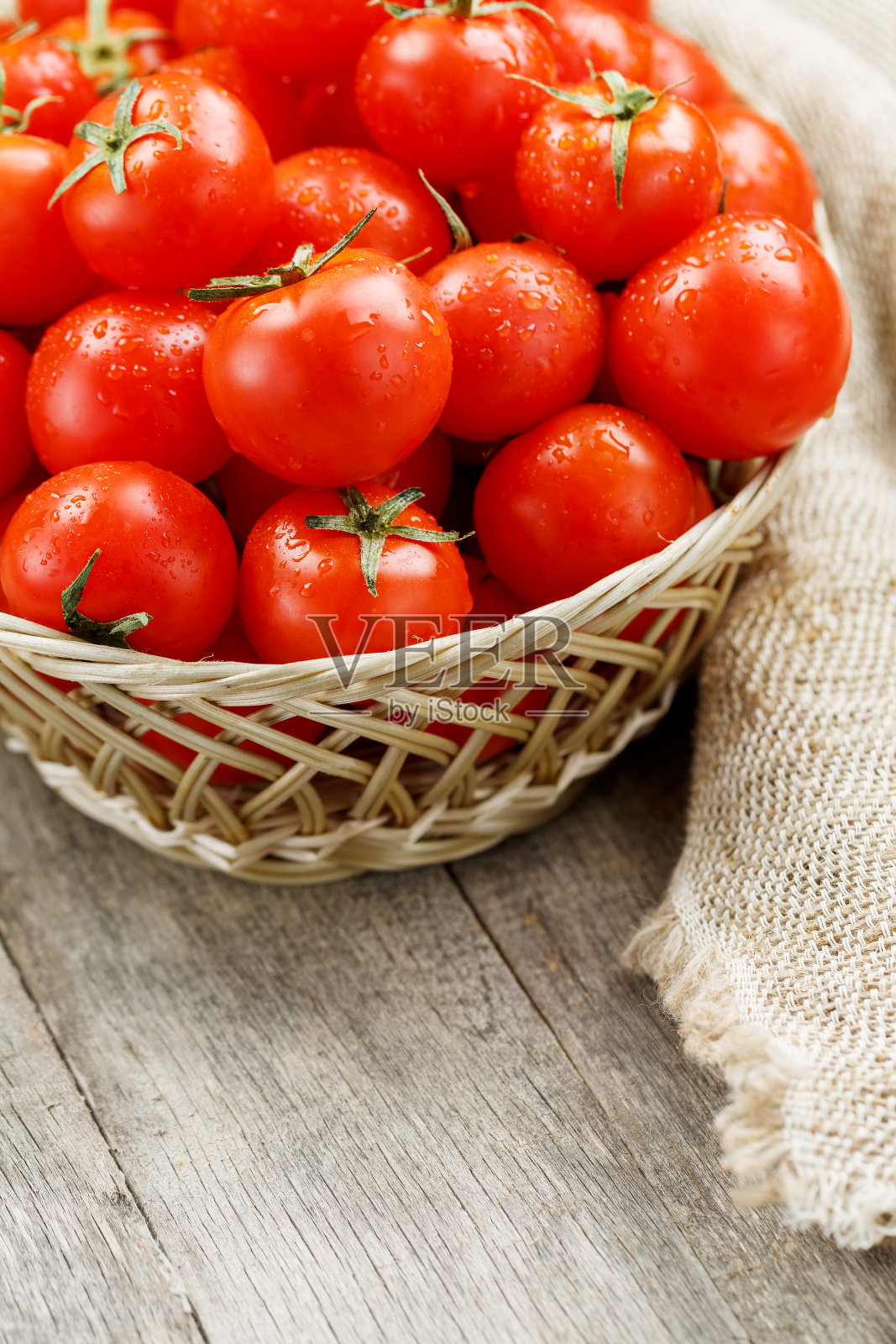 旧木桌上的柳条篮子里装着红色的小西红柿。熟透多汁的樱桃照片摄影图片