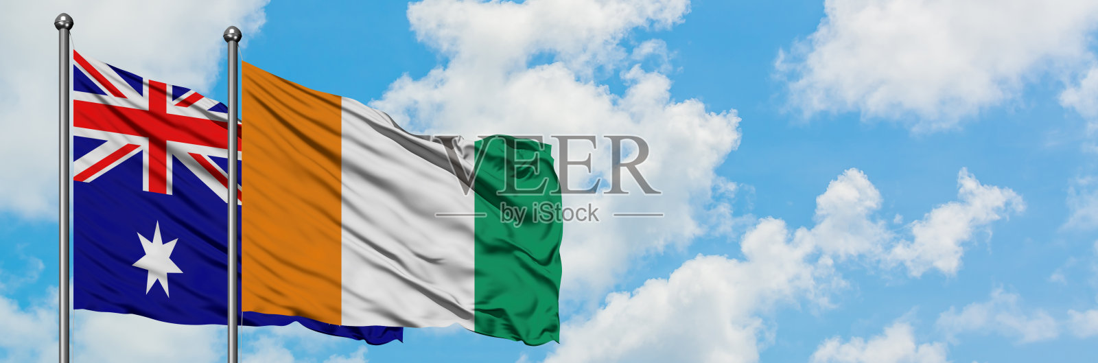 澳大利亚和科特迪瓦的国旗在风中飘扬，对抗着白色多云的蓝天。外交理念，国际关系。照片摄影图片