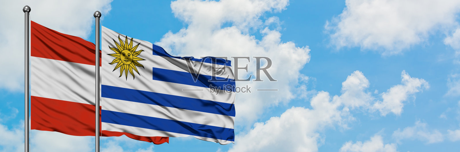 奥地利和乌拉圭的国旗一起在风中飘扬，对抗着白色多云的蓝天。外交理念，国际关系。照片摄影图片