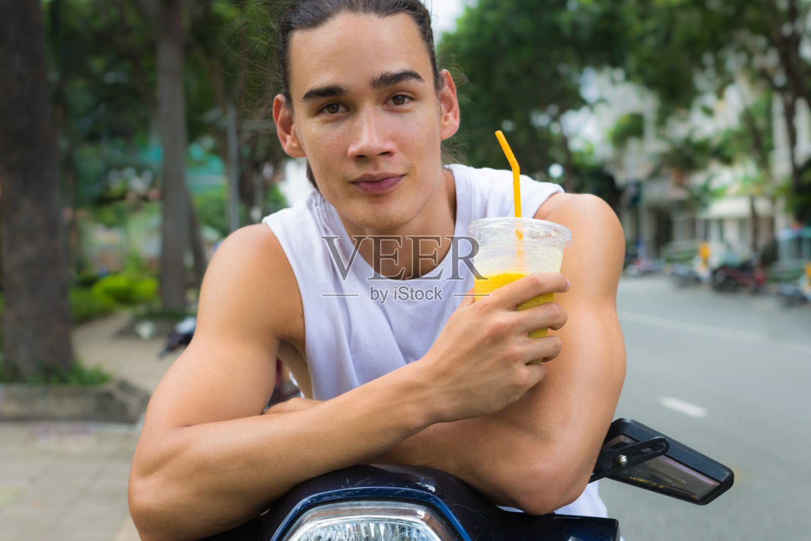 一个年轻人的肖像拿着水果饮料，而休息在一个助力车上照片摄影图片