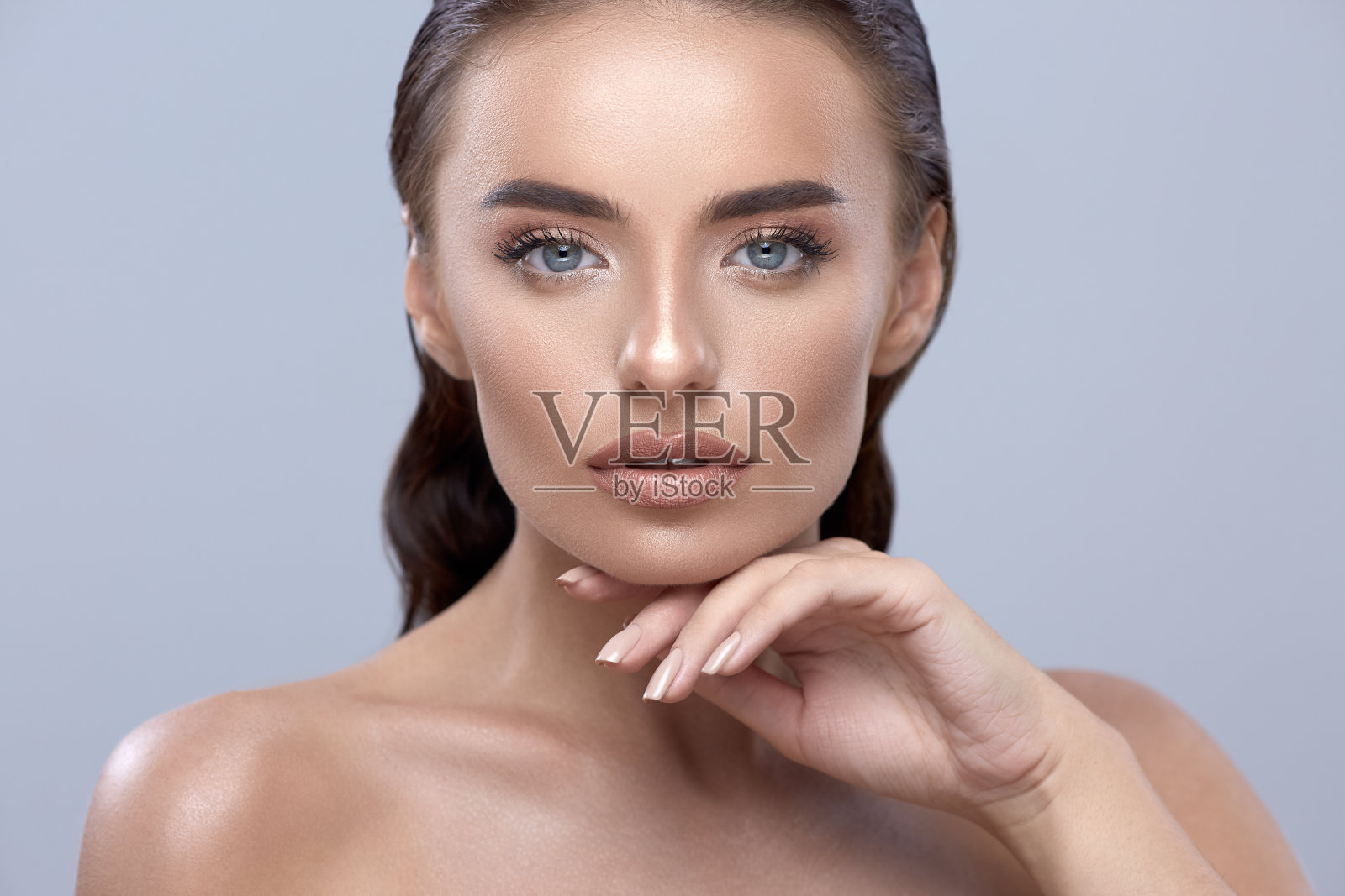 年轻的女孩在灰色的背景触摸脸，美丽的女孩特写，黑发模特看着相机，美丽的脸与手臂照片摄影图片