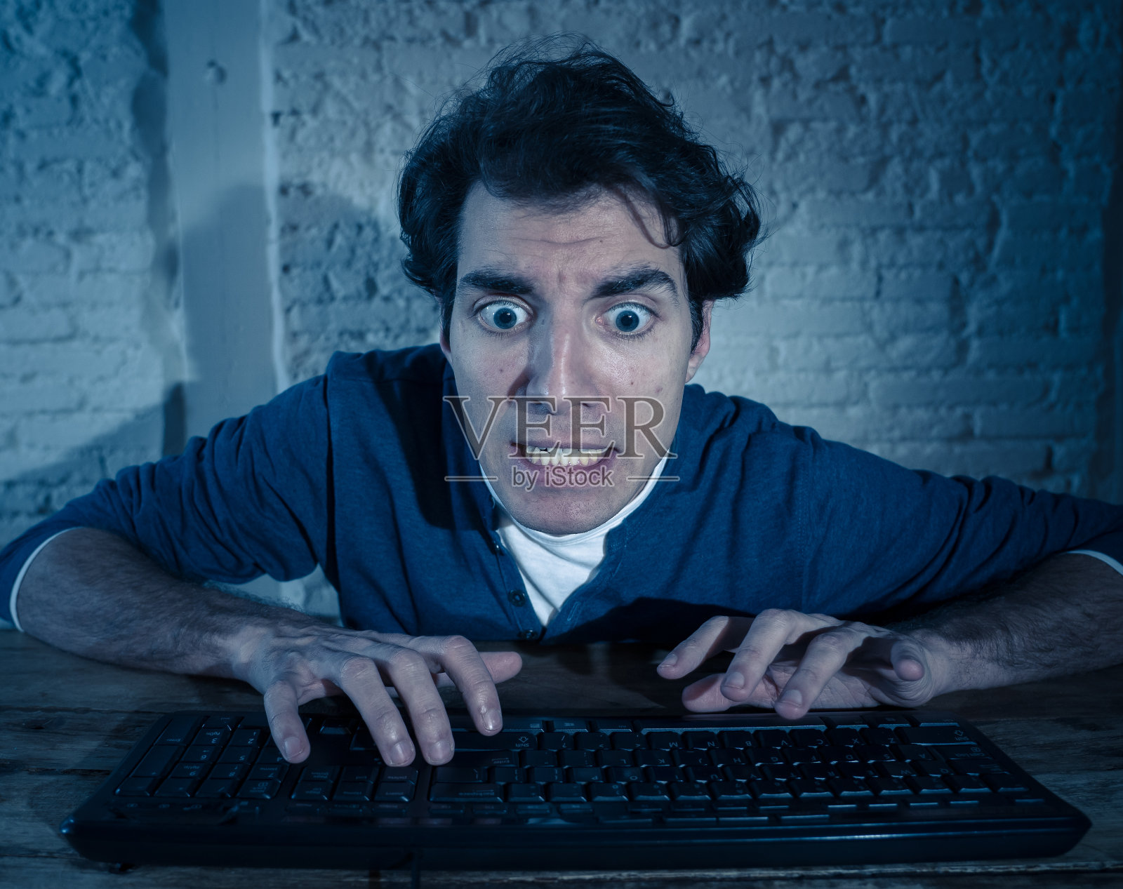 沉迷的年轻人在晚上独自在电脑笔记本电脑上感到压力和不堪重负，试图完成工作或赢得在线游戏或赌博。工作狂和网络技术成瘾。照片摄影图片