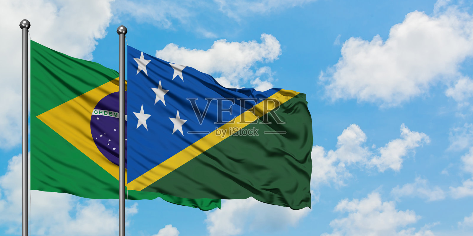 巴西和所罗门群岛的国旗一起在风中飘扬，对抗着白色多云的蓝天。外交理念，国际关系。照片摄影图片