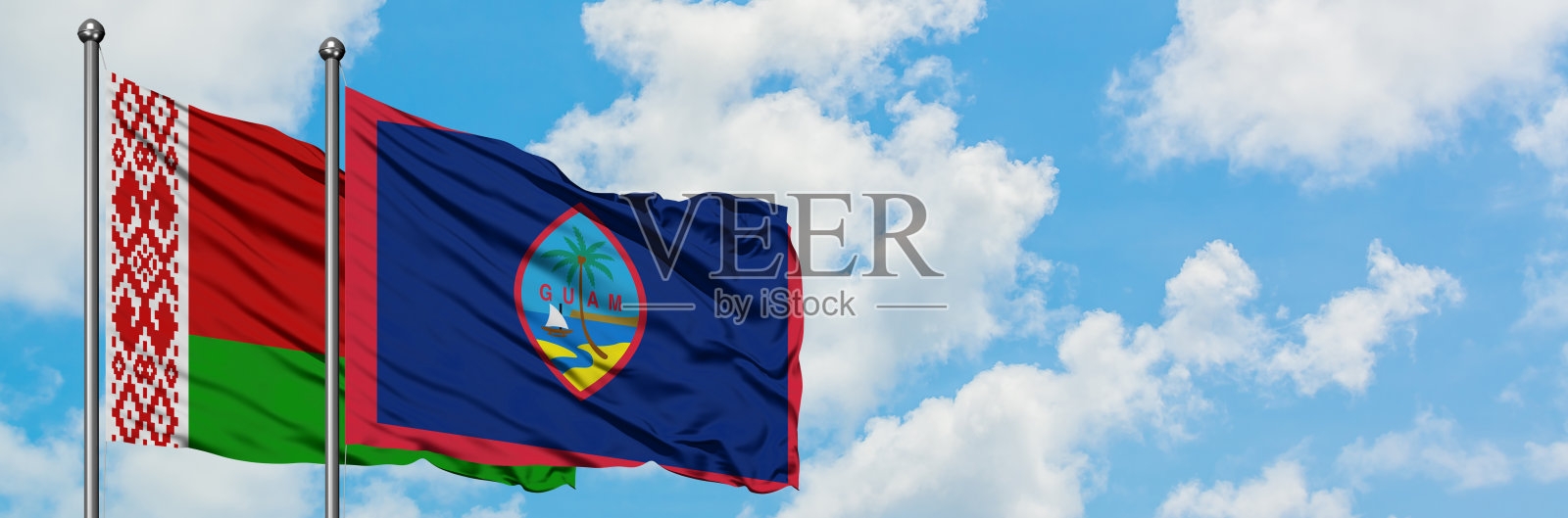 白俄罗斯和关岛的国旗在风中飘扬，对抗着白云般的蓝天。外交理念，国际关系。照片摄影图片