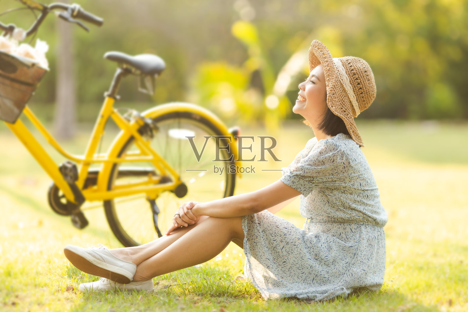 年轻的亚洲女子穿着蓝色的连衣裙坐在草地上，面带微笑，女性露营对夏季的概念照片摄影图片