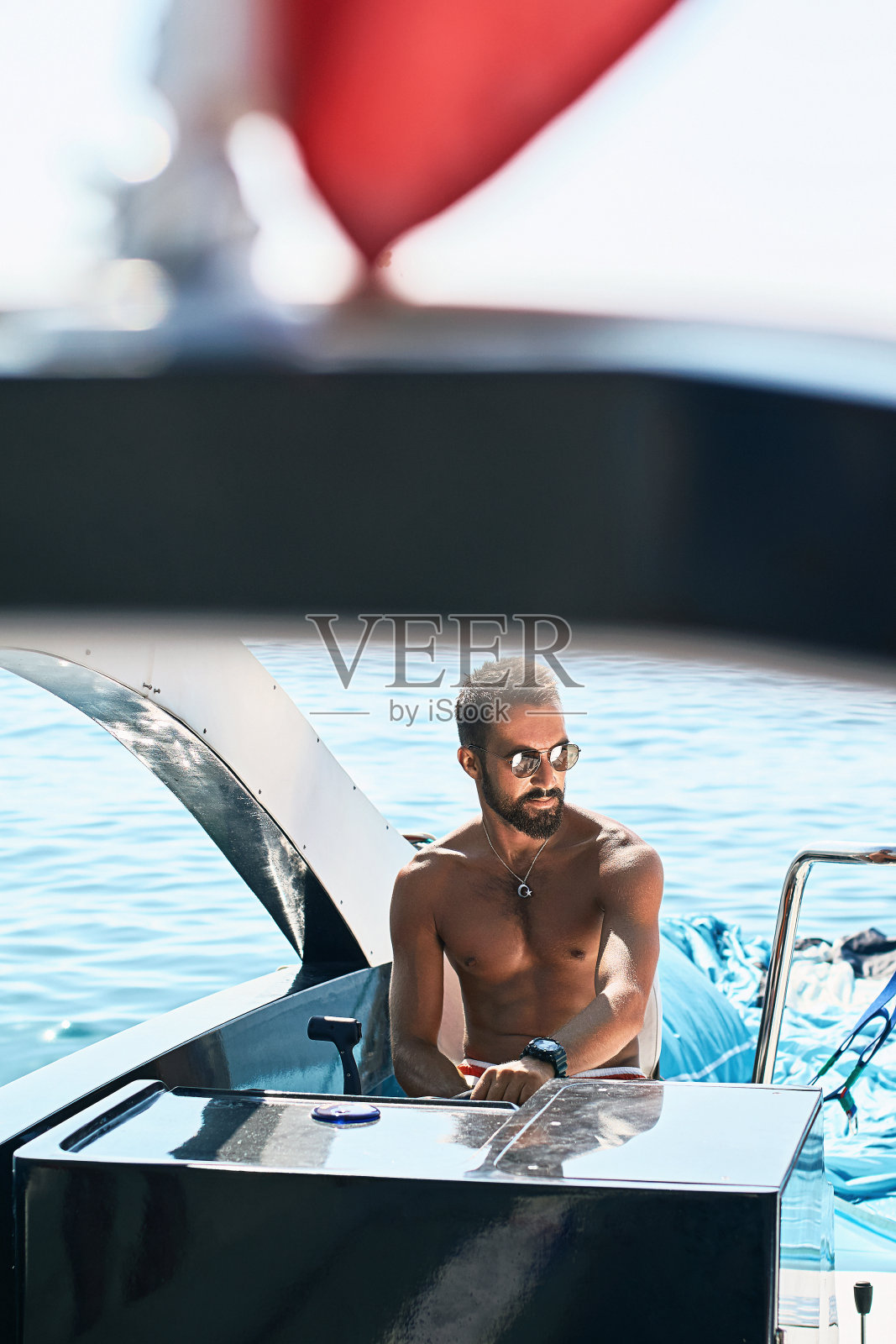 晒黑的年轻英俊的穆斯林船长掌舵游艇，红旗下控制面板照片摄影图片