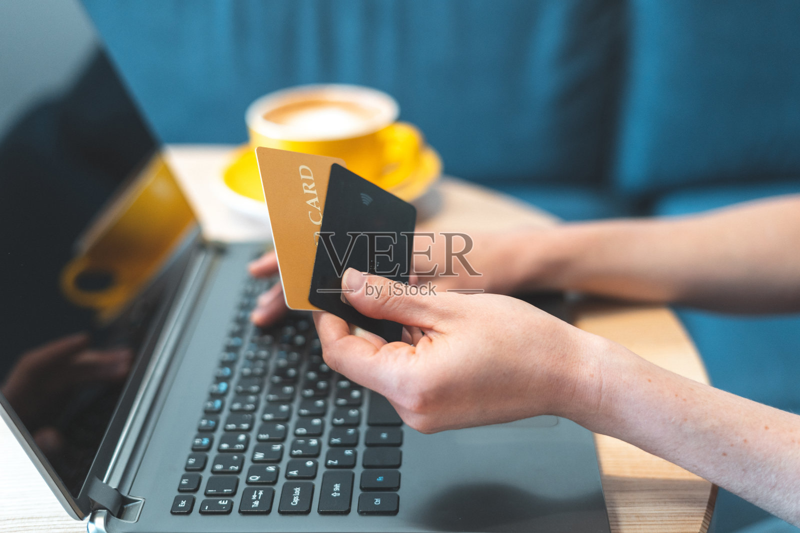 裁剪的照片的成年女孩或年轻的女人花周末在舒适的咖啡馆舒适和现代室内明亮的光线房间。女性用电脑用两张银行卡进行网上购物照片摄影图片