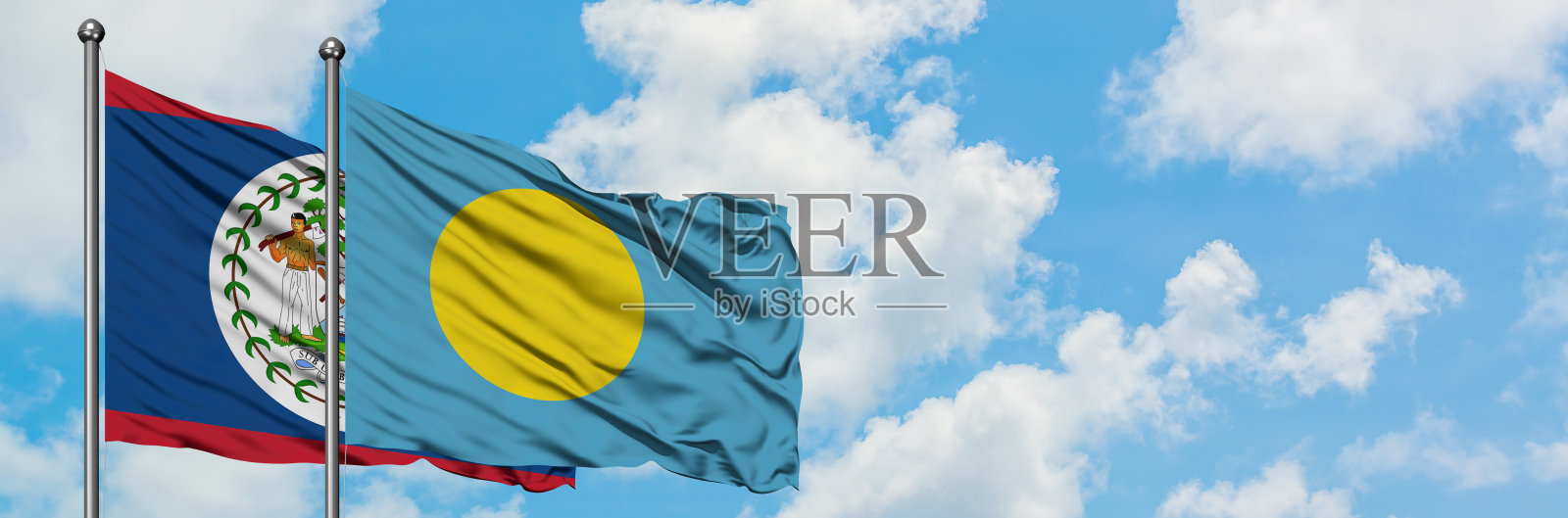 伯利兹和帕劳的国旗在风中飘扬，对抗着白色多云的蓝天。外交理念，国际关系。照片摄影图片