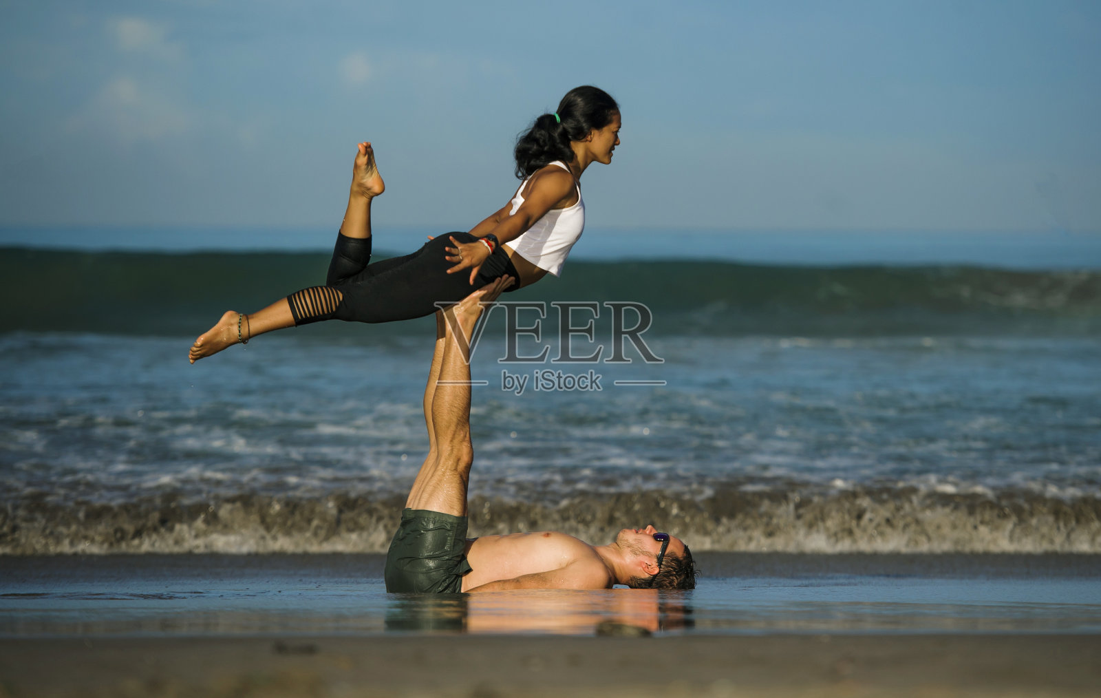 年轻迷人和集中的杂技演员练习跨越瑜伽平衡和冥想练习在美丽的海滩在蓝天下的心灵和身体控制和健康的生活方式照片摄影图片