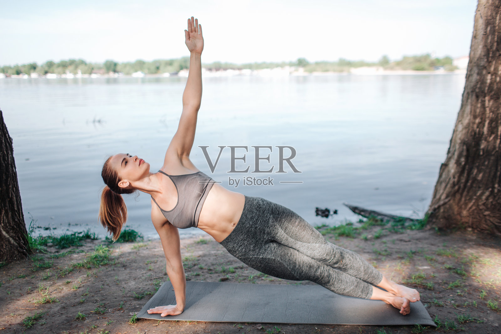 好女孩一只手站着另一只手在空中。她也抬起头来。女孩在河边伸展。照片摄影图片