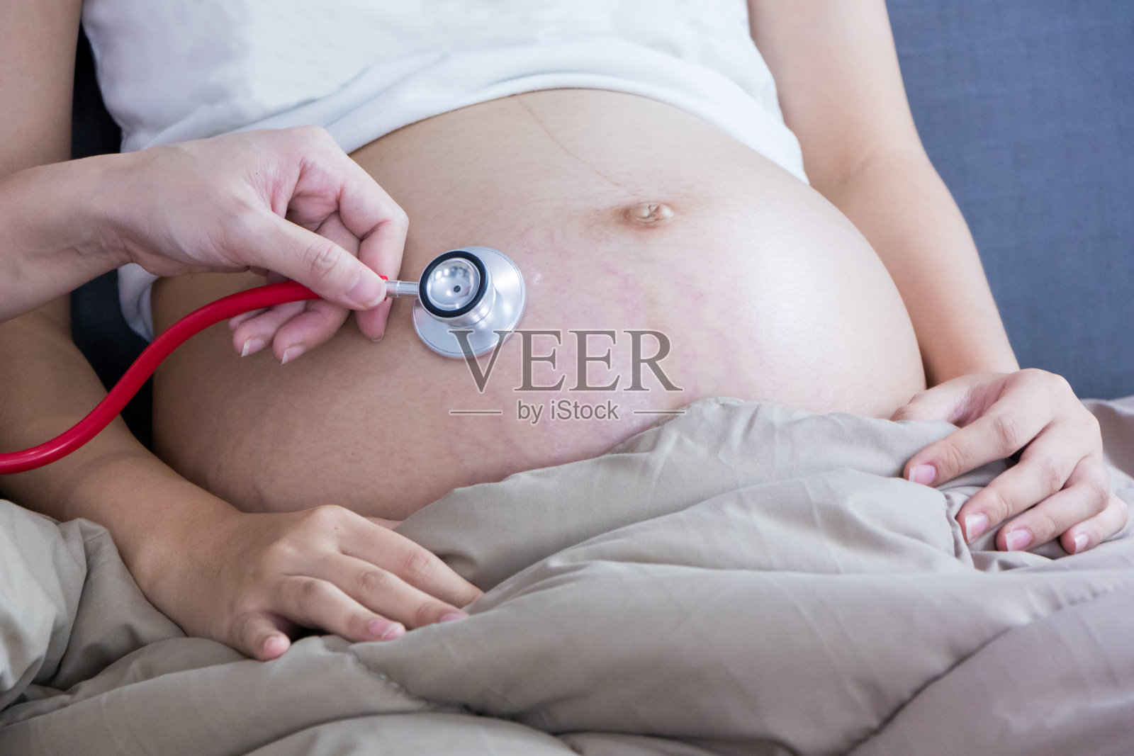 美丽的年轻孕妇肖像使用听诊器听她的肚子。怀孕保健为婴儿概念做准备。少女母亲中的母性。照片摄影图片