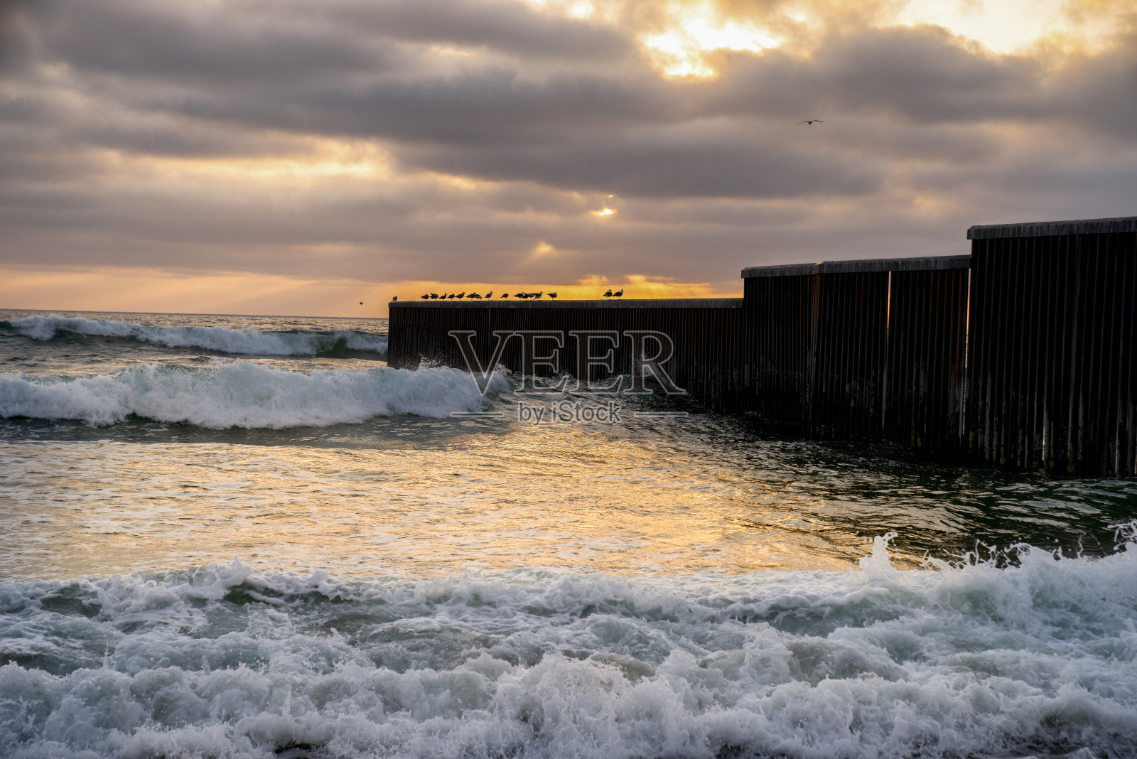 海滩和海浪的近景日落附近的国际边界墙在Playas Tijuana，墨西哥照片摄影图片