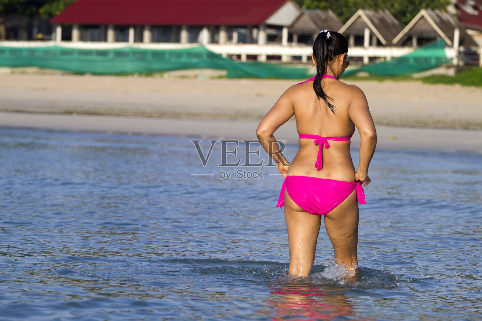 穿着粉红色比基尼的女人走在海滩上照片摄影图片