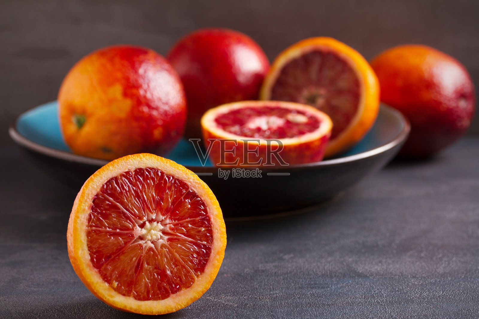 灰色背景下，蓝色碗里的血或红橙。新鲜成熟的柑橘类水果照片摄影图片