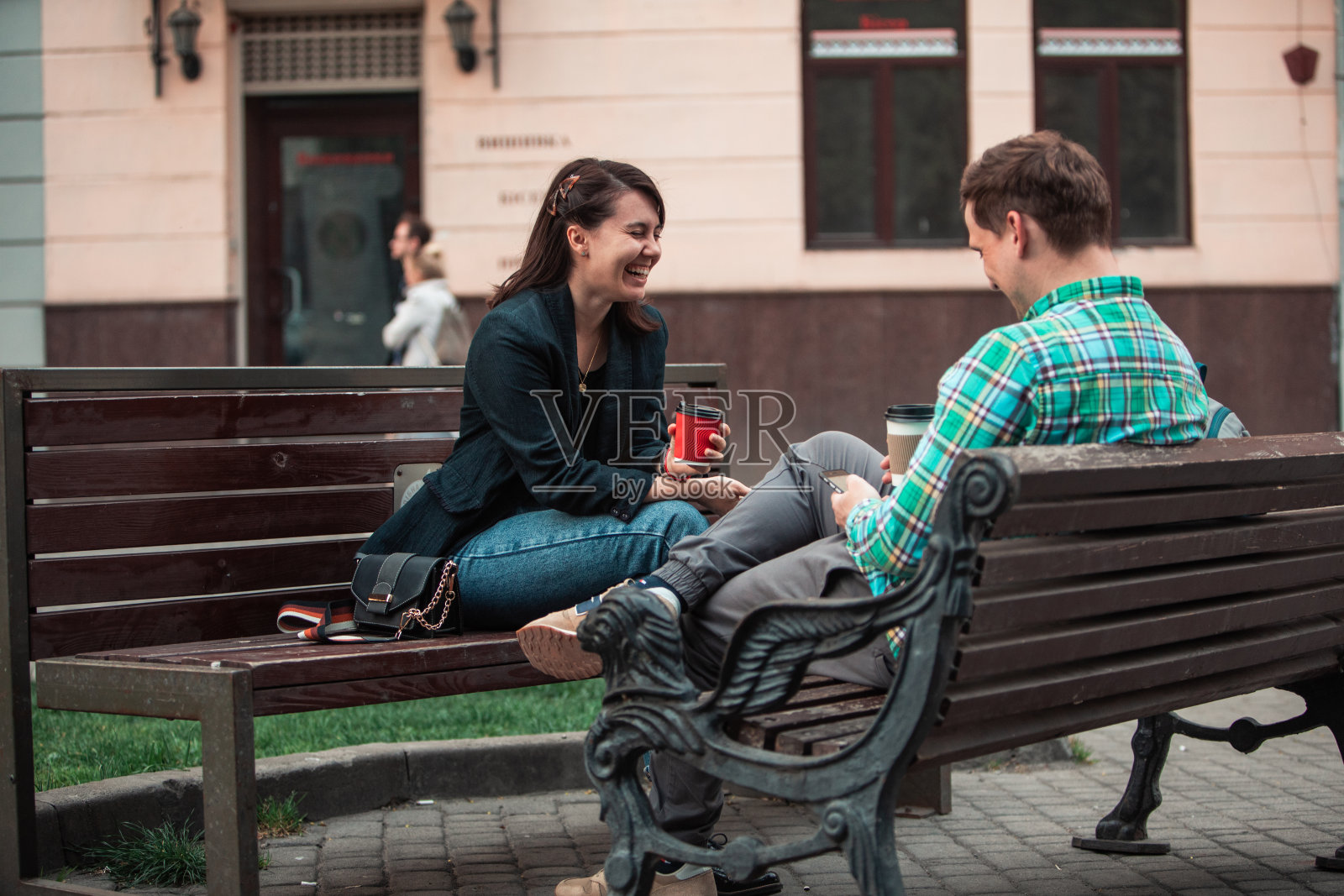 谈笑风生的男人和女人坐在长椅上喝着咖啡上网。城市的生活方式照片摄影图片