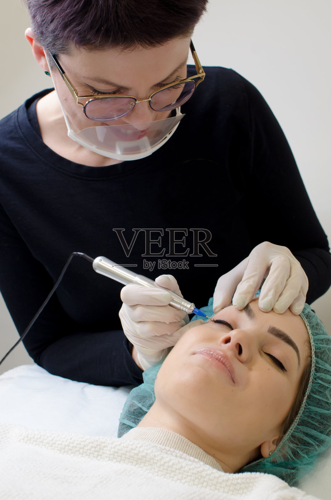 微笑迷人的美容师应用永久化妆眼线，照片摄影图片