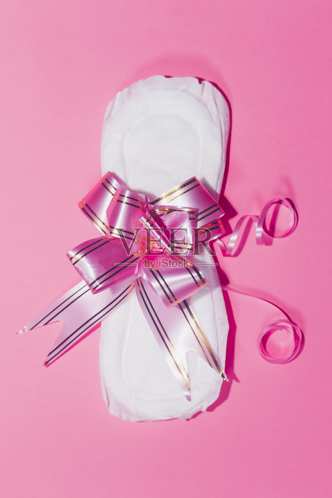 粉色背景上系着丝带的卫生巾。医学、女性保健和排卵观照片摄影图片