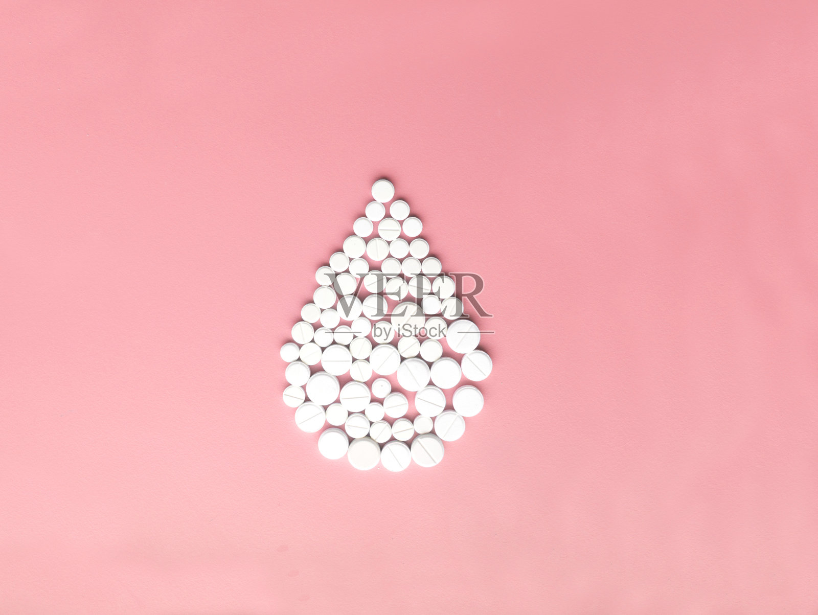 粉红色背景上白色药丸制成的血滴。照片摄影图片