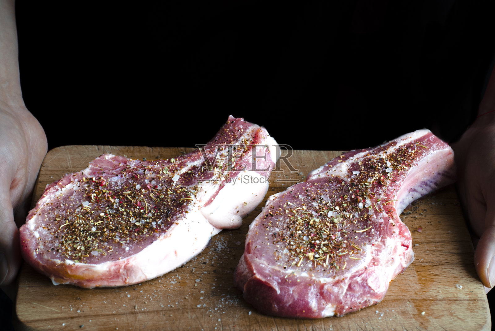 手上拿着一块板，板上放着两块撒了香料的生猪肉，准备烹饪照片摄影图片