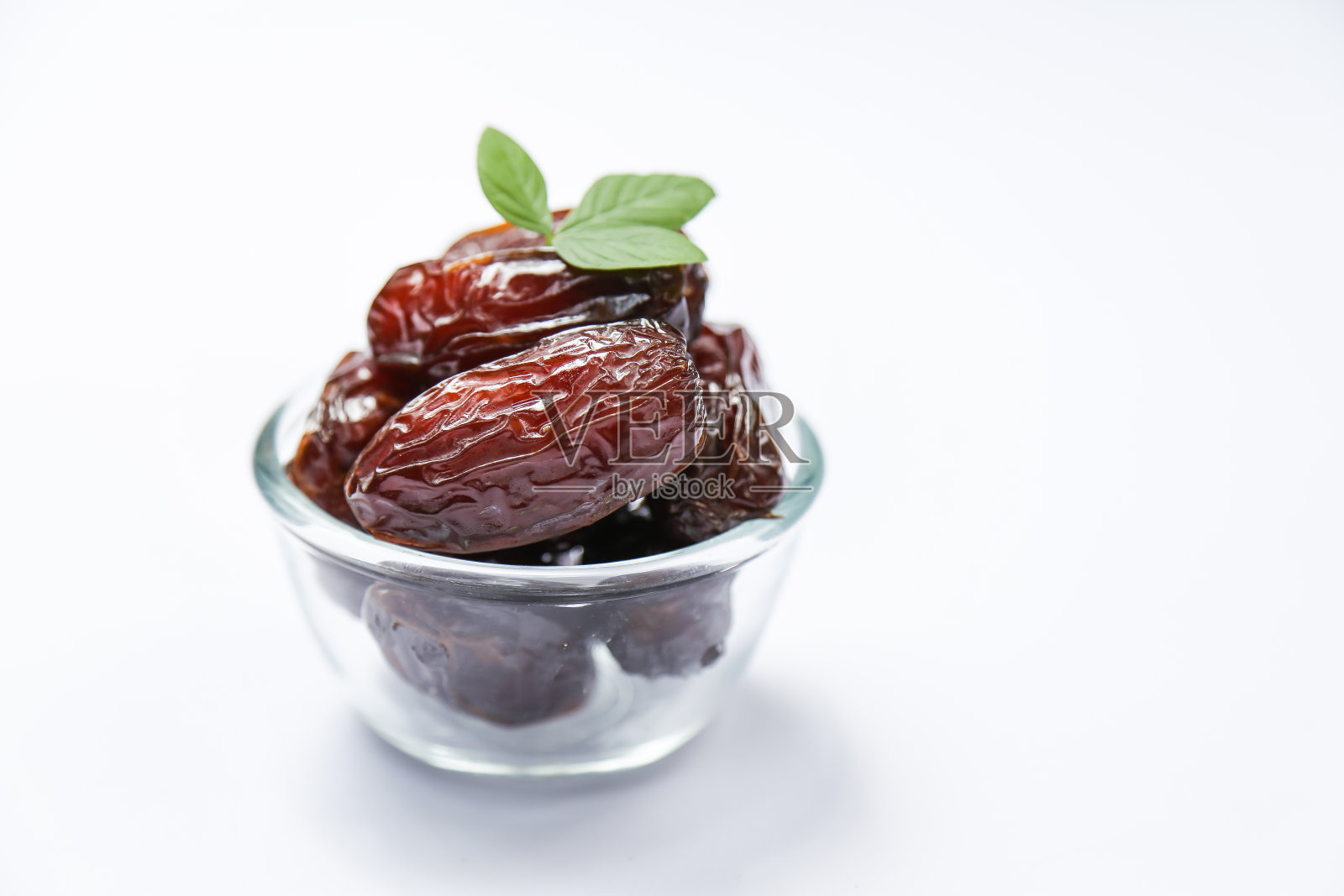 许多椰枣被放在一个透明的玻璃碗里，背景是白色的照片摄影图片