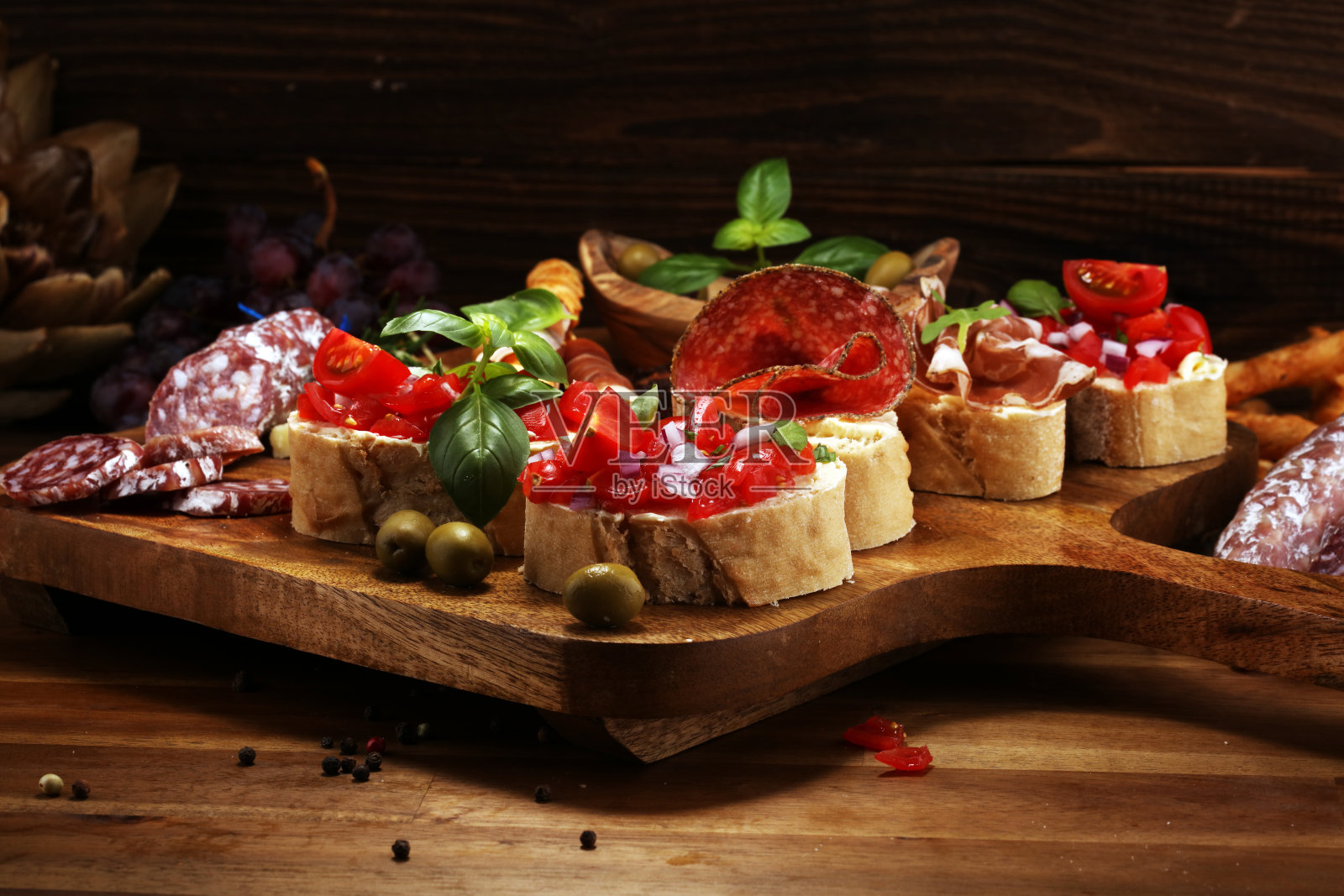 各种开胃前菜。切菜板与意大利熏火腿，意大利腊肠，奶酪，面包和橄榄在深色木制背景照片摄影图片