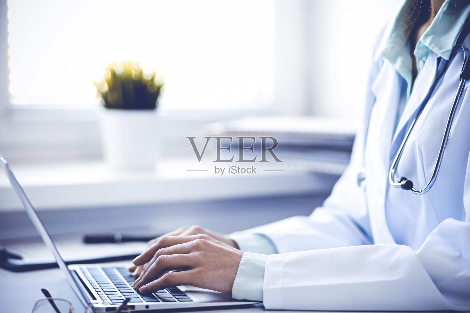 在医院里，一名女医生坐在靠窗的桌子前使用笔记本电脑。医学保健理念。绿色是主色调照片摄影图片