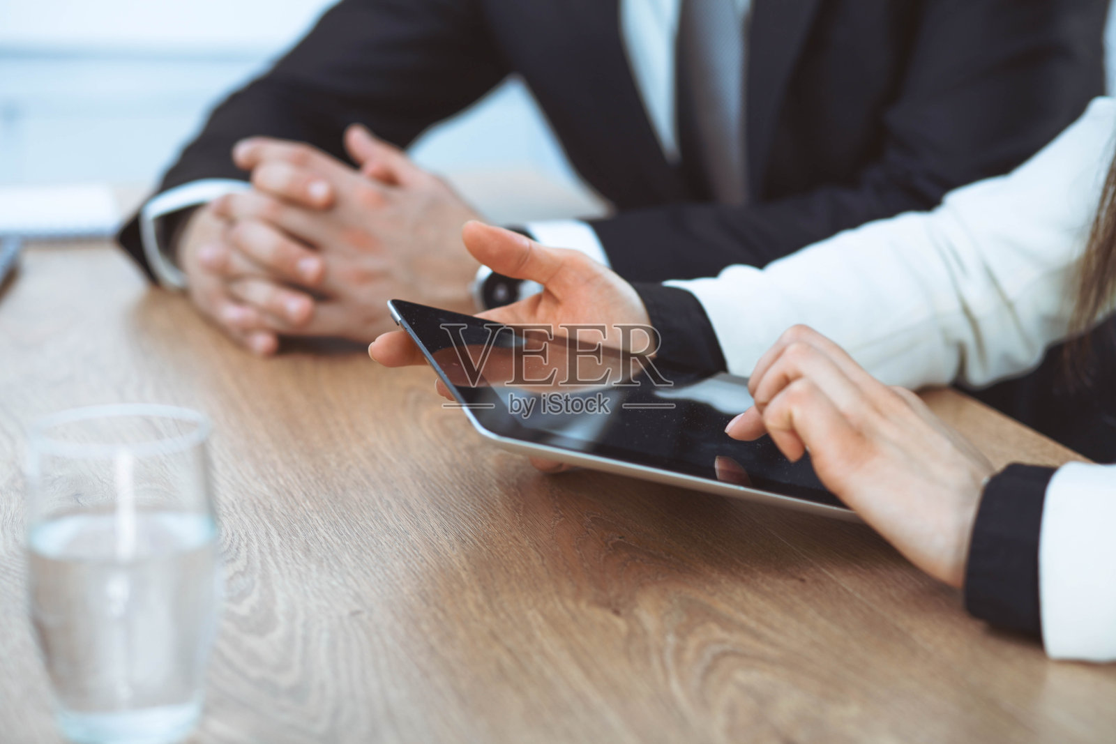 一群商务人士或律师在办公室开会时一起工作，双手使用平板电脑并做特写笔记。谈判与沟通概念照片摄影图片