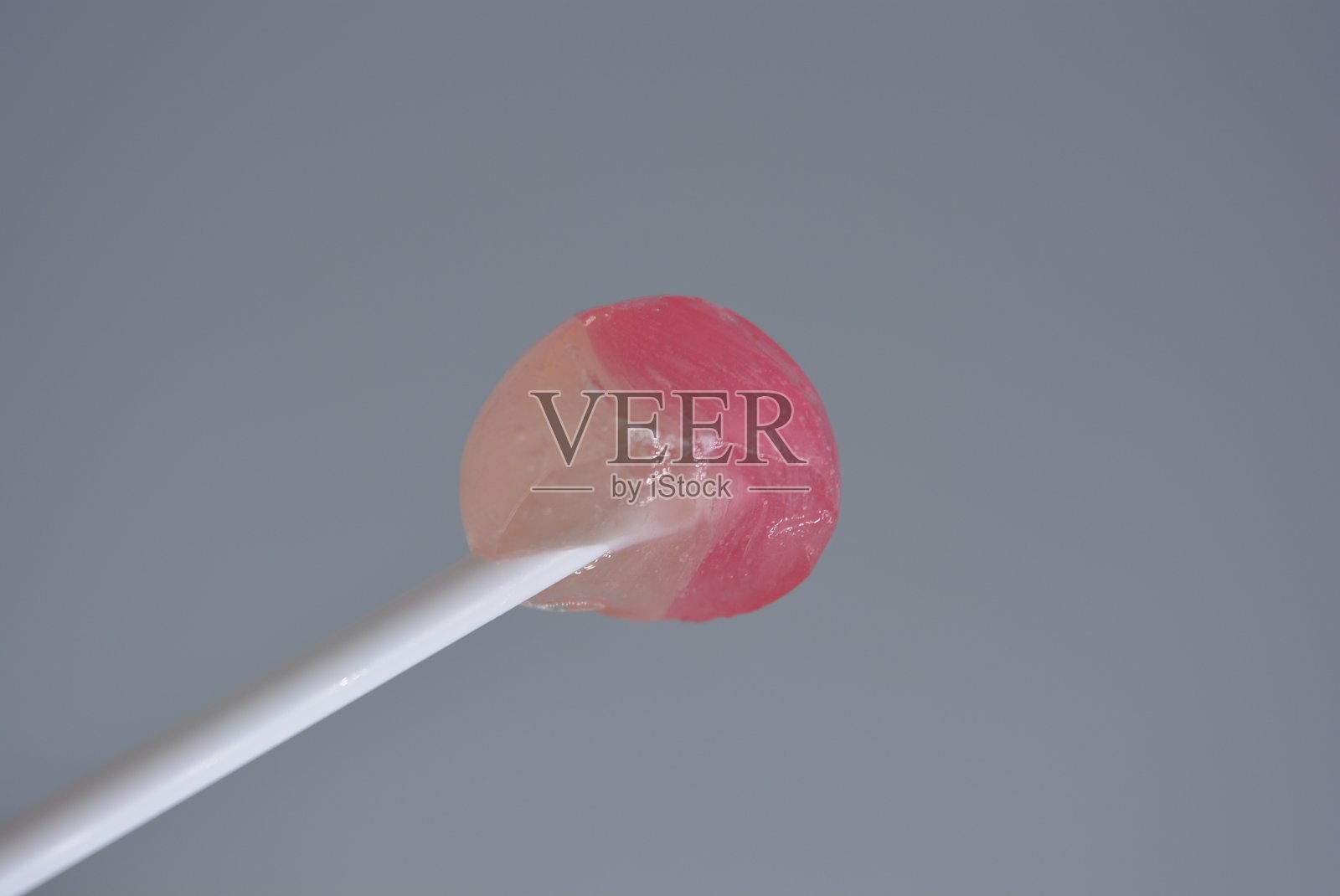 被咬过的甜糖果，圆圆的吮着的糖果放在白色的白色塑料棒上，白色的背景上，啾啾，啾啾。照片摄影图片