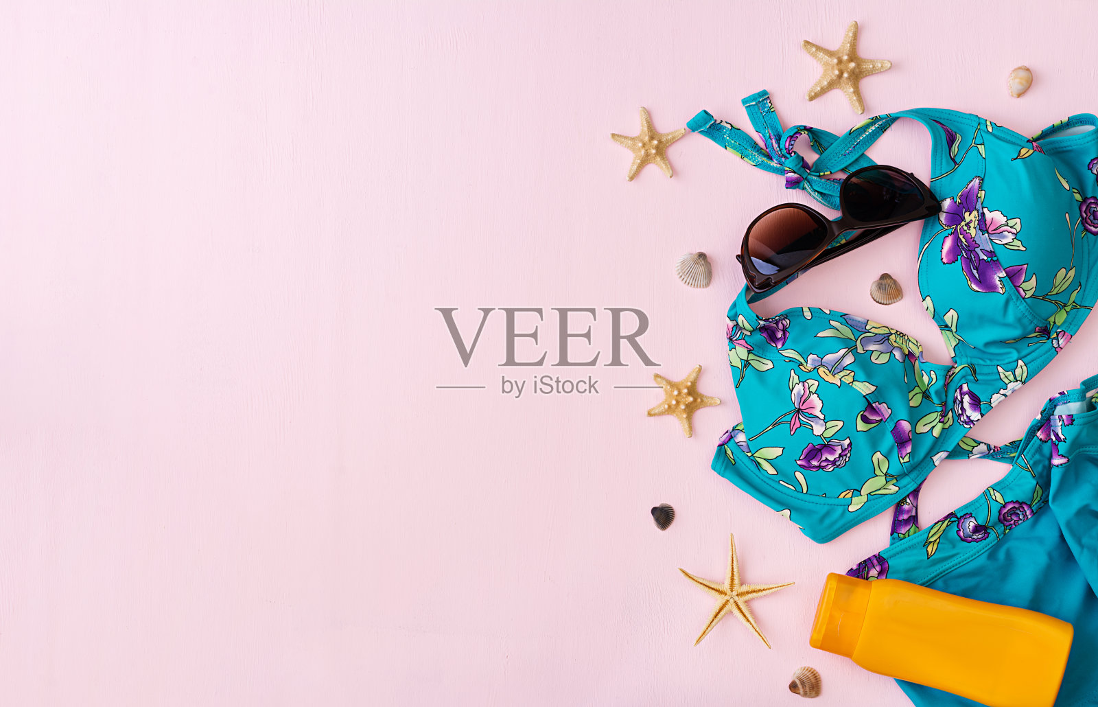 粉红色背景上有不同贝壳和海星的泳衣。俯视图照片摄影图片