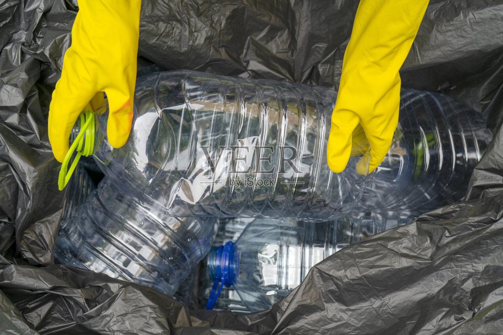 男人收集垃圾。手把塑料瓶放在塑料垃圾袋里。照片摄影图片