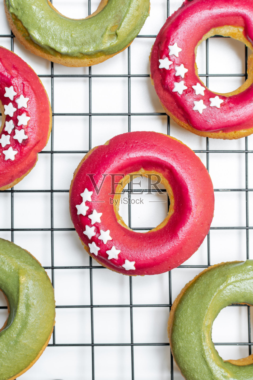 烘烤最小概念-俯视图的新鲜烤甜甜圈与明亮的粉红色和绿色糖霜，星星洒在冷却架照片摄影图片