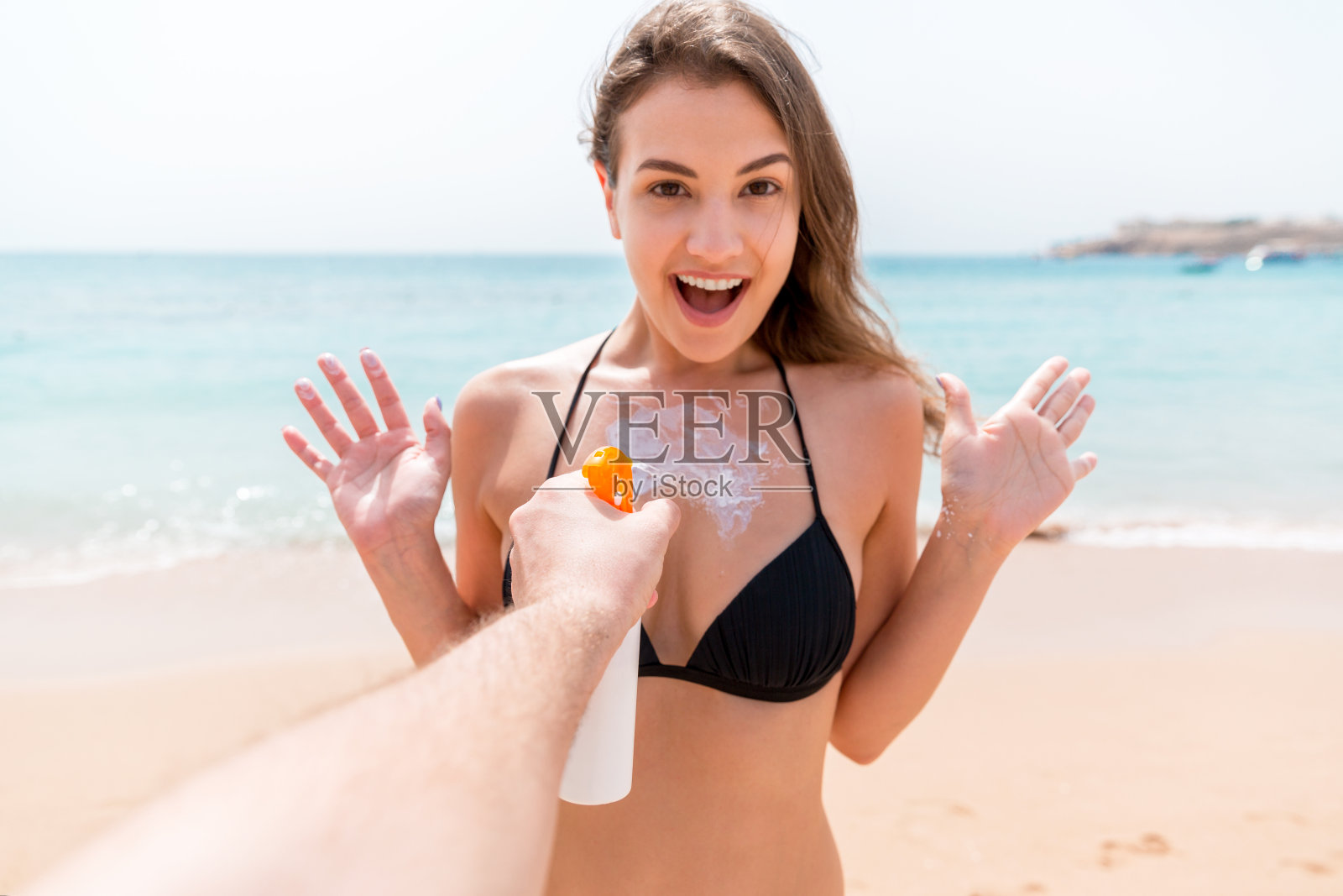 在海滩上，男人突然在惊讶的女人的胸部涂抹防晒霜照片摄影图片