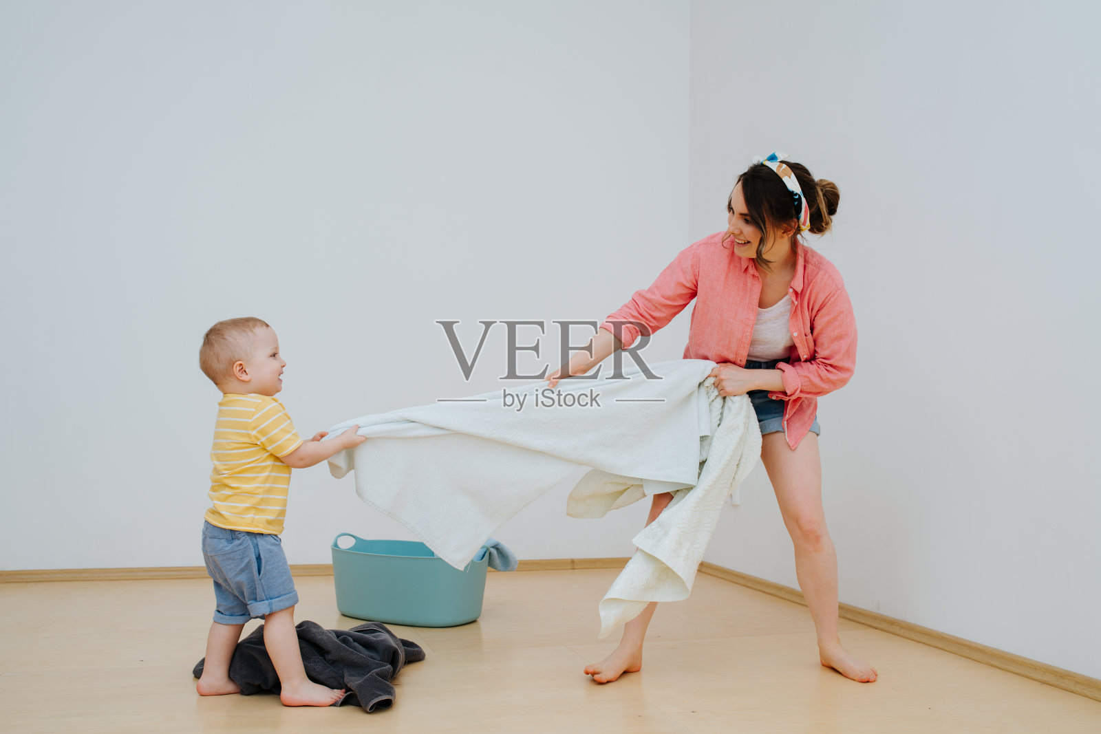 快乐的蹒跚学步的儿子和他的母亲正在用毛巾玩拔河游戏照片摄影图片