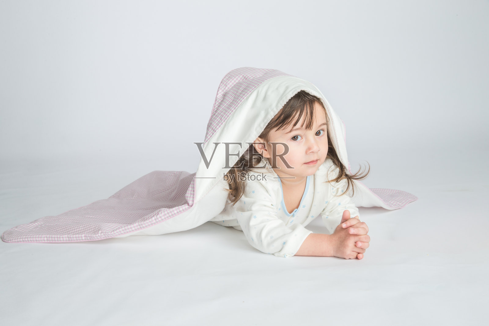 一个小女孩穿着家装，盖着婴儿毯，婴儿躺在地板上。水平的照片。浅灰色背景照片摄影图片