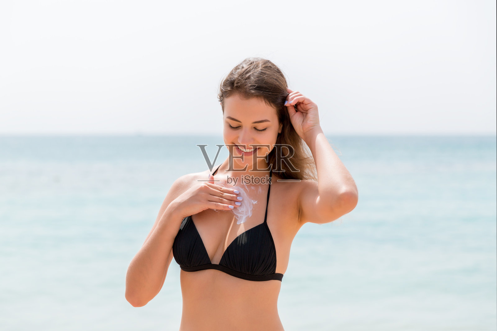 年轻漂亮的女子在阳光明媚的海滩上用防晒霜保护胸部皮肤照片摄影图片