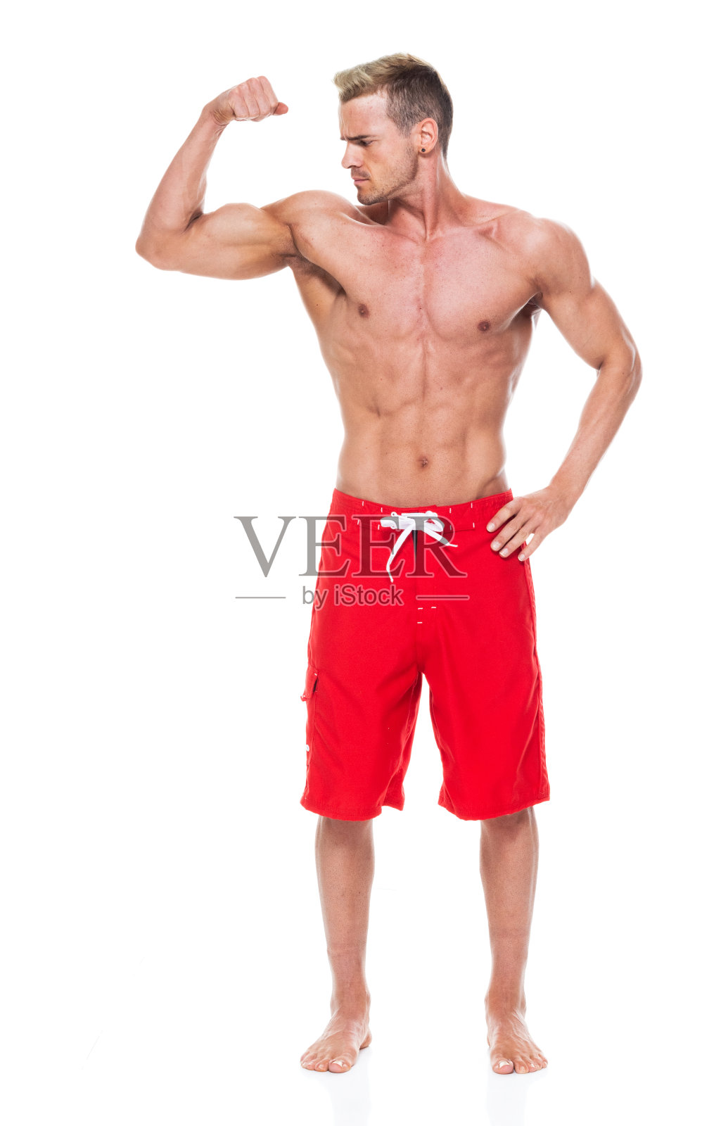 英俊的肌肉男子谁是赤膊和穿着板短裤和弯曲他的肌肉照片摄影图片