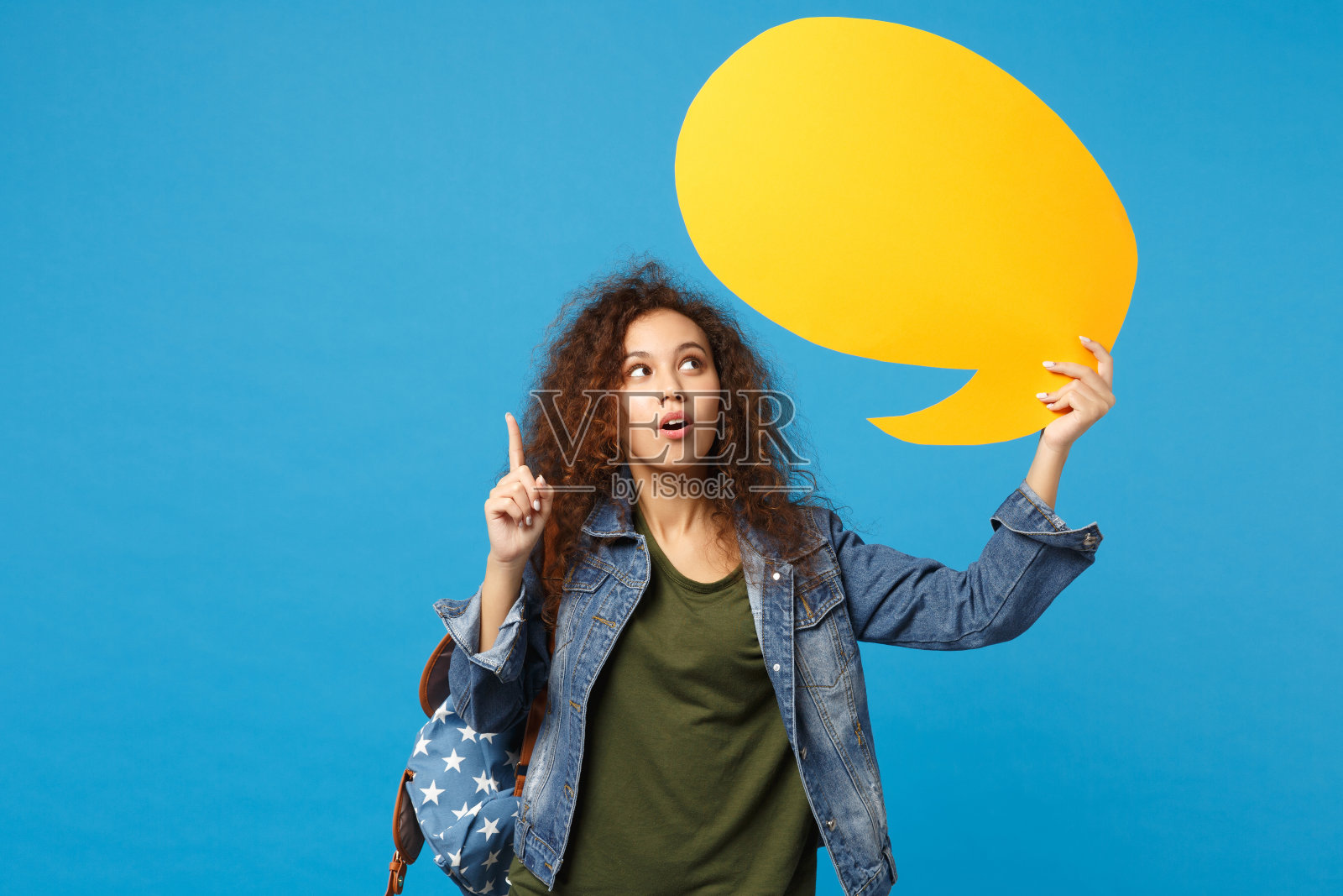 年轻的非洲裔美国女孩十几岁的学生在牛仔衣服，背包说云孤立在蓝色背景的工作室肖像。中学教育中的大学学院观念。模拟拷贝空间。照片摄影图片