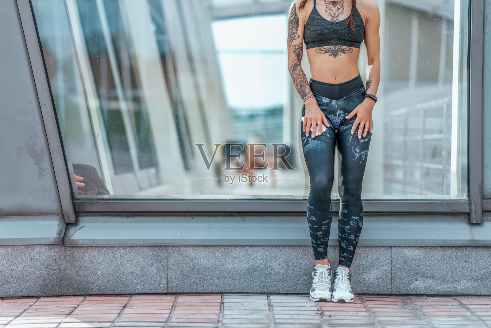 女孩立玻璃柜，夏日都市女子健身运动，积极生活青春。动力，成就，成功。自由空间。手机纹身，健身手环运动服，打底裤，顶级运动鞋。照片摄影图片