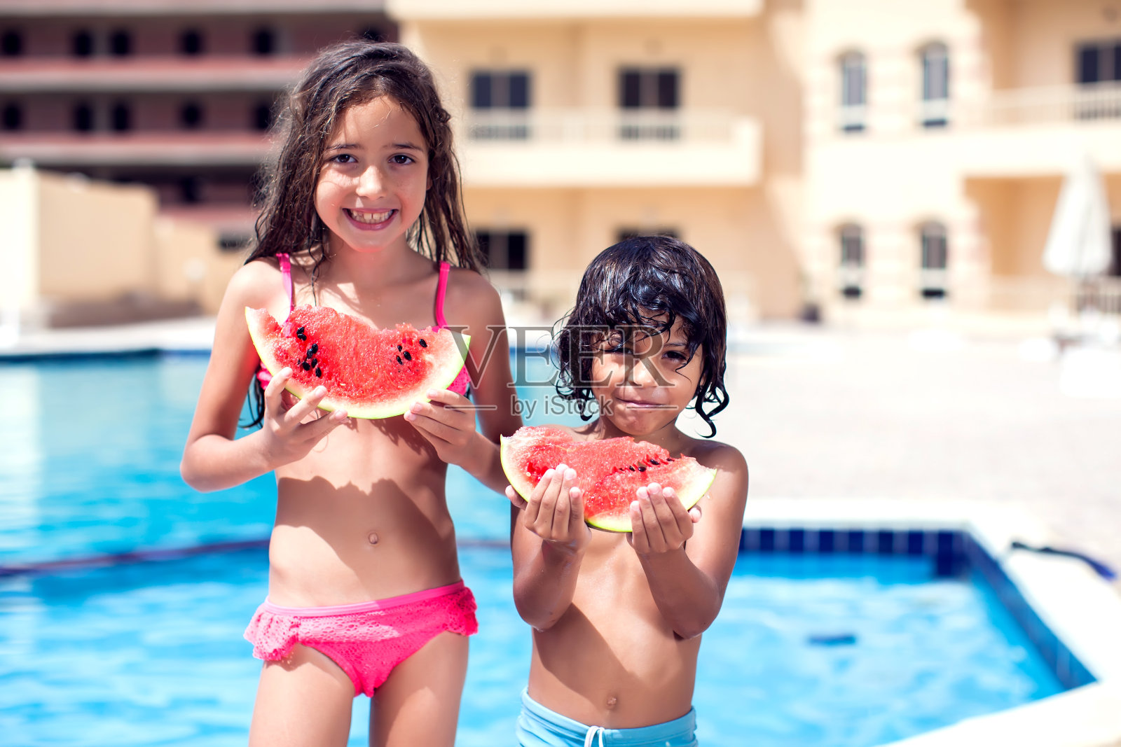 小男孩和小女孩在游泳池里吃西瓜。儿童与夏季概念照片摄影图片