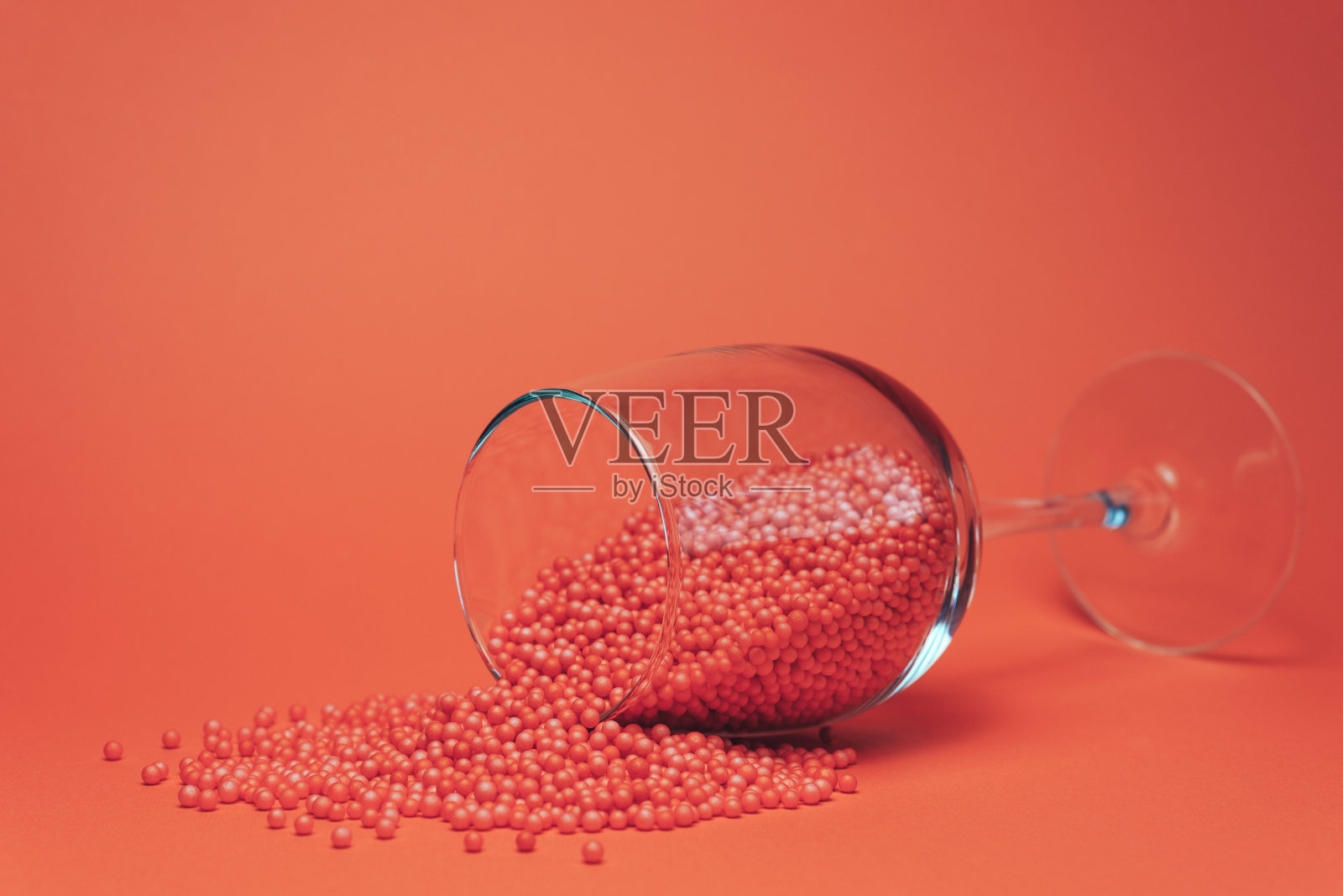 葡萄酒杯与红色小球假葡萄酒(合成，不是有机，准备，刺激)在美丽的珊瑚橙色背景。照片摄影图片