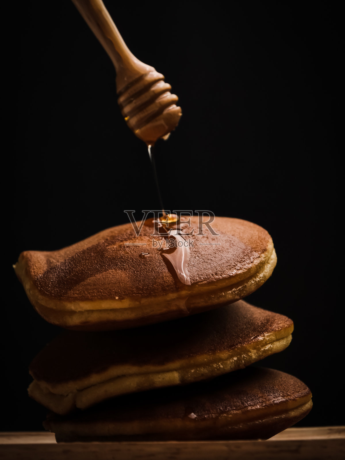 煎饼与蜂蜜糖浆勺和黑色背景。照片摄影图片