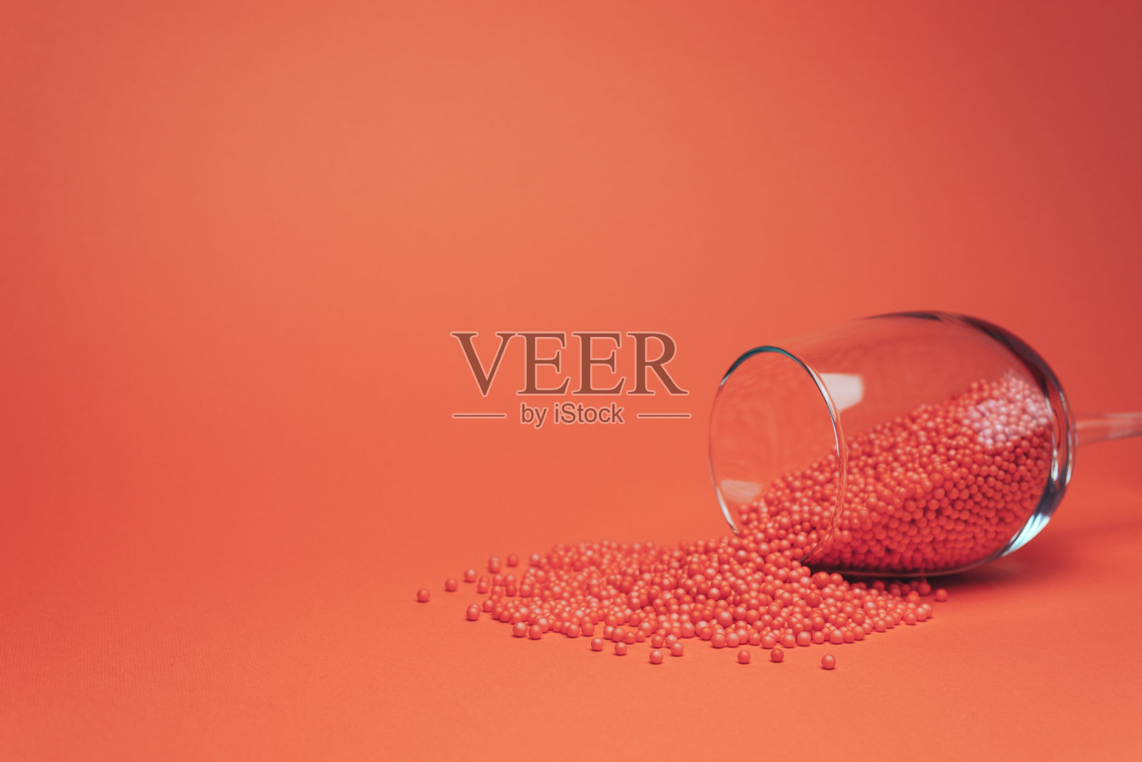 葡萄酒杯与红色小球假葡萄酒(合成，不是有机，准备，刺激)在美丽的珊瑚橙色背景。照片摄影图片