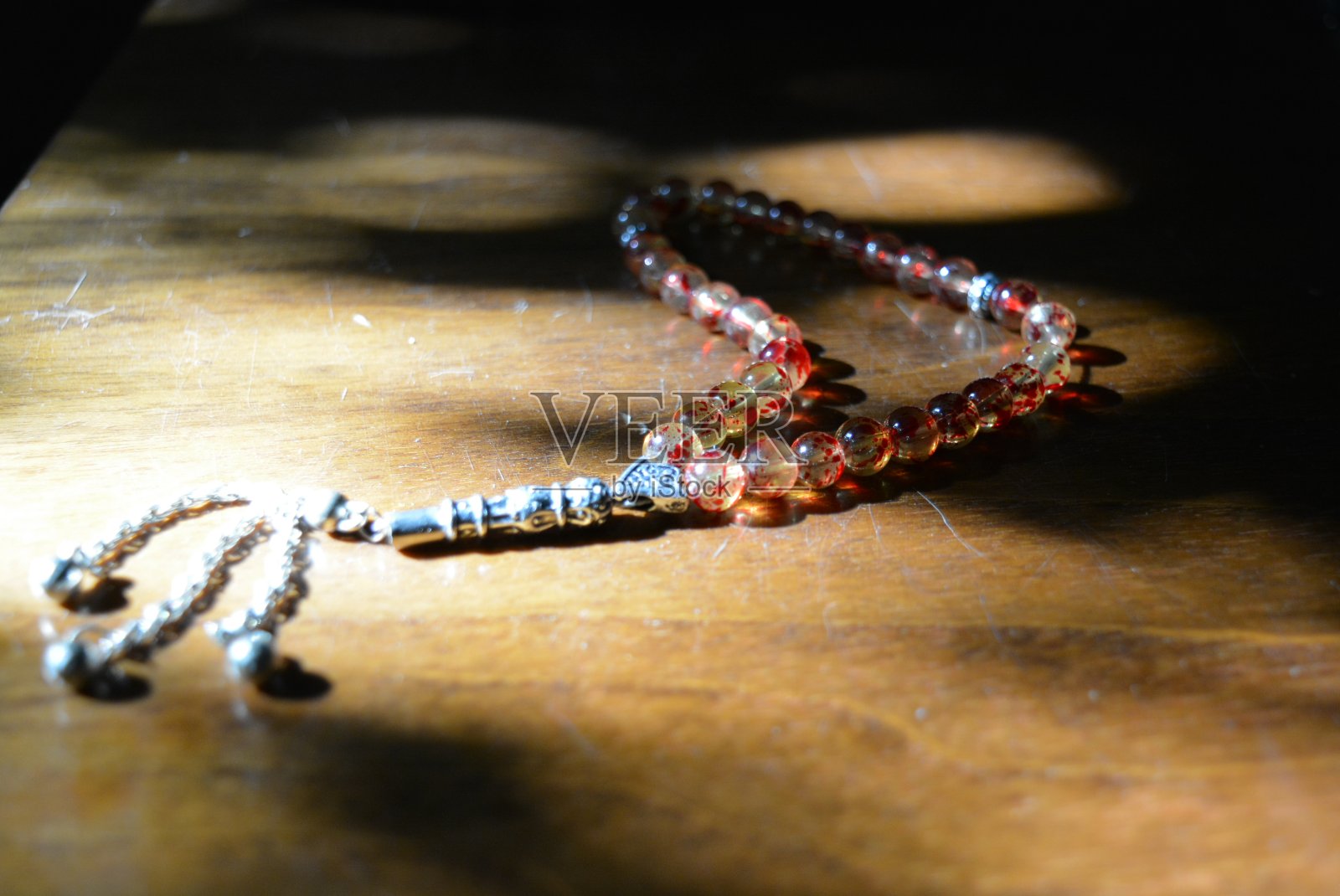 在阳光的照射下，老式漆木桌上的黄色和红色的穆斯林宗教珠。照片摄影图片