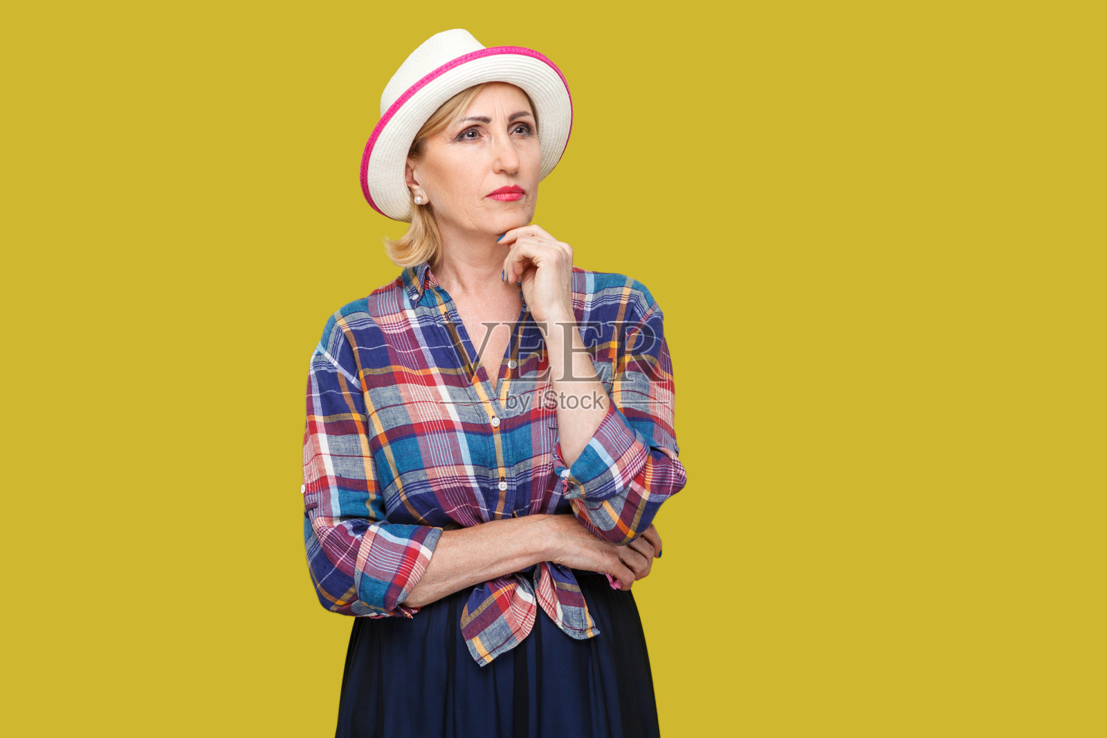 严肃周到的现代时尚成熟女性肖像，以休闲风格与白色帽子站立，触摸她的下巴，询问和思考该做什么。照片摄影图片