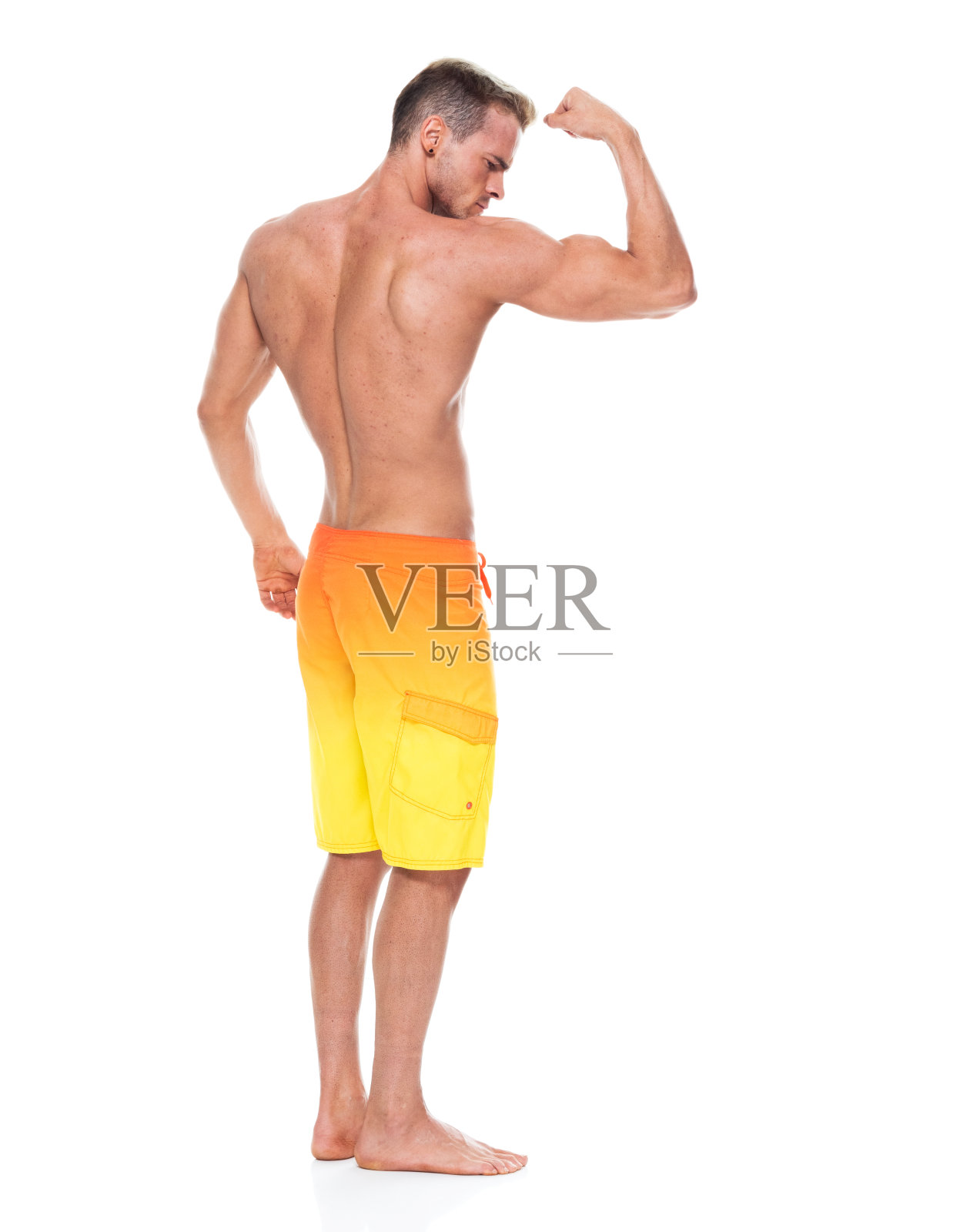 英俊的肌肉男子谁是赤膊和穿着板短裤和弯曲他的肌肉照片摄影图片