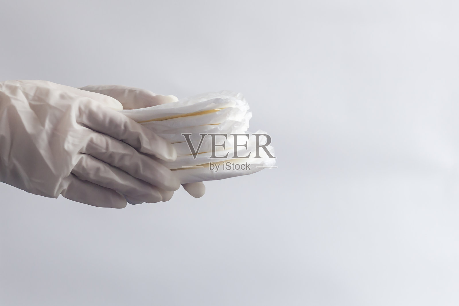 女性卫生产品。女人的手在医疗手套拿着一堆卫生巾对白色的背景。月经日概念表示女性月经周期。照片摄影图片