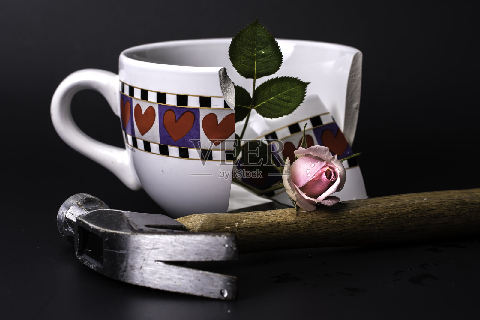 破碎的心杯与得到粉碎与锤子和粉红色的玫瑰在黑色的背景照片摄影图片